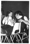 Male and female sit with feet up on chairs; both hold hands up to chest in conversation