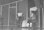 Male actor sits in chair while female dusts behind another chair by George Fox University Archives