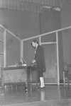 Actor stands at desk with small item in hand by George Fox University Archives
