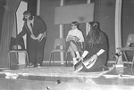 Students sit on stage in chairs and on rug doing various things