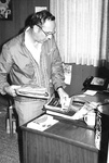Ron Crecelius moves books and paper on desk by George Fox University Archives