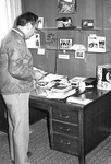 Ron Crecelius moves books and paper on desk by George Fox University Archives