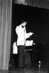 Male in white suit reads off paper into microphone