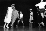 People in eclectic clothes run and dance in circle around briefcase by George Fox University Archives